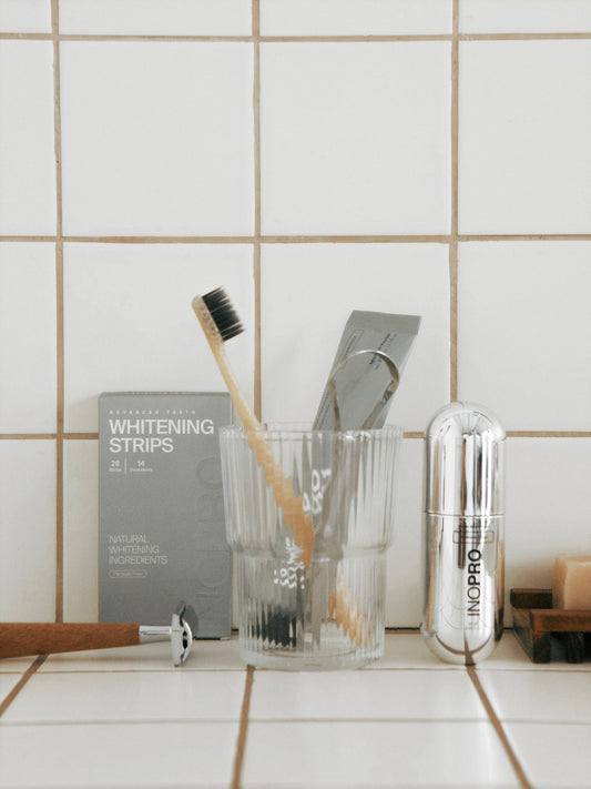 INOPRO toothpaste, foam mouthwash and whitening strips on a tiled bathroom counter