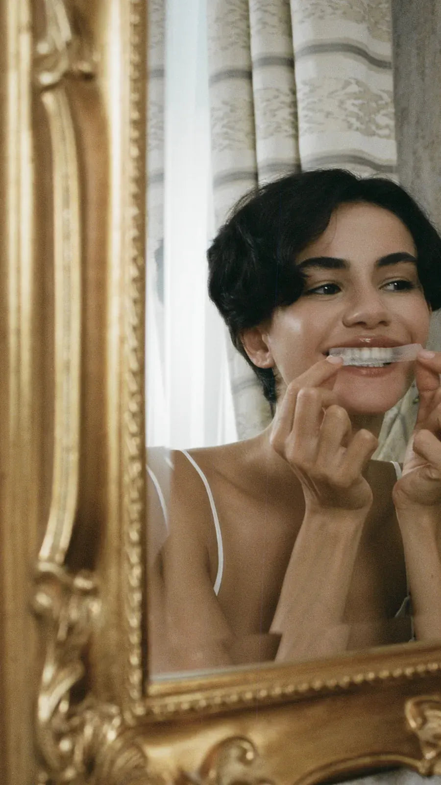 Woman applying a whitening strip in an ornate mirror