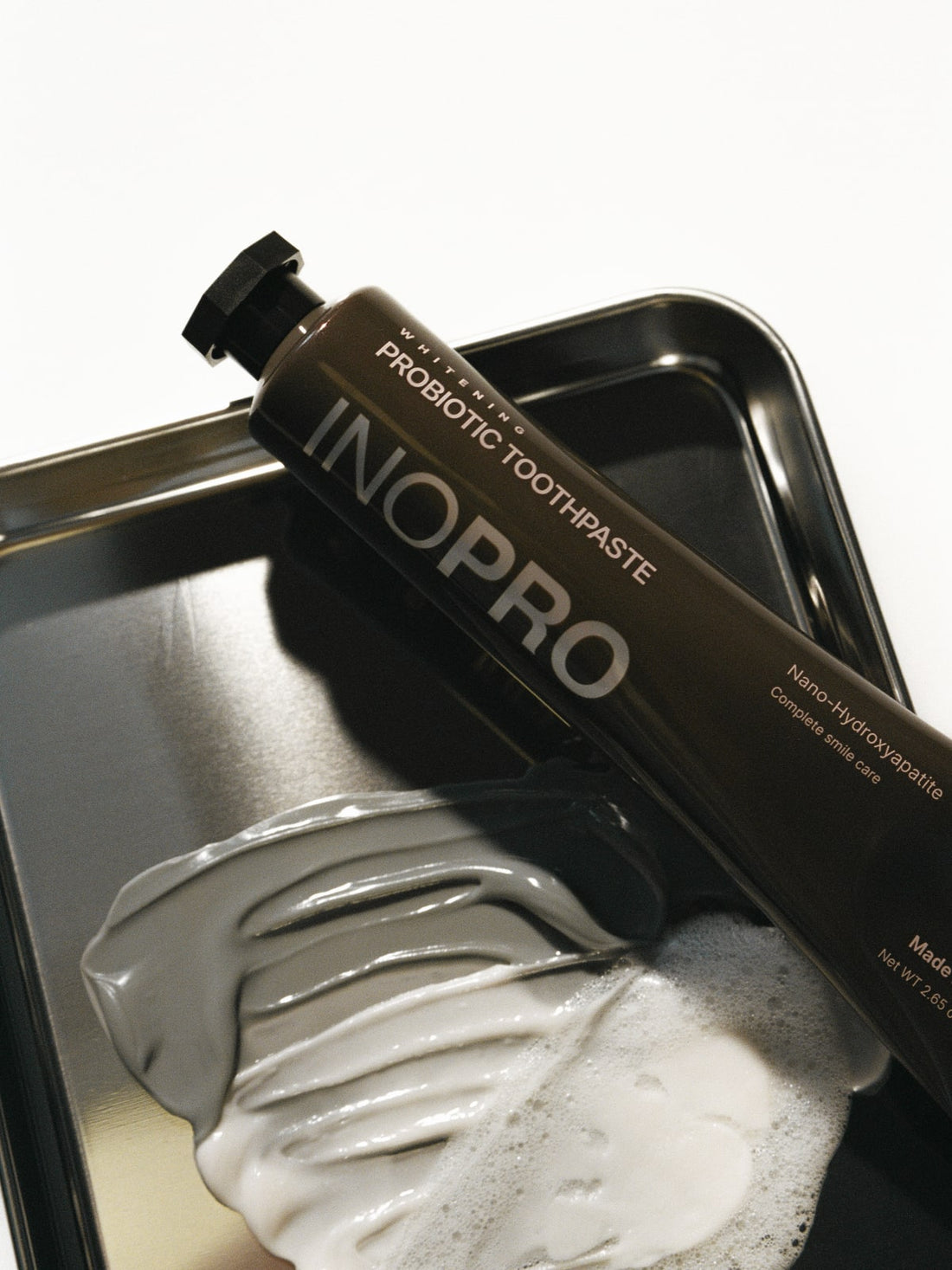 INOPRO probiotic toothpaste on a silver tray beside a creamy toothpaste texture